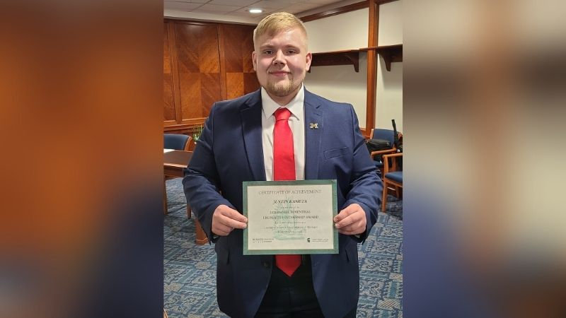 Justin Kasieta in a navy suit holding a Certificate of Achievement at the Michigan State Capitol